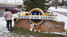 Students stand at the sign of Oxford High School where memorial items are being placed in Oxford, Mich., Wednesday, Dec. 1, 2021. A 15-year-old sophomore opened fire at the school, killing several students and wounding multiple other people, including a teacher.
