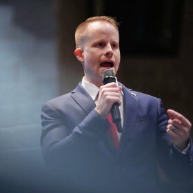 A man in a suit speaks into a microphone.