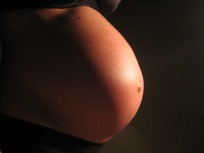 A very pregnant belly is in spotlight against a dark brown background.