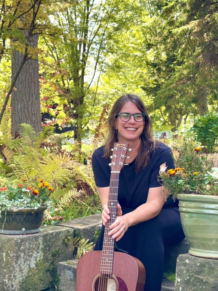 A woman sits in a natural green space with an acoustic guitar