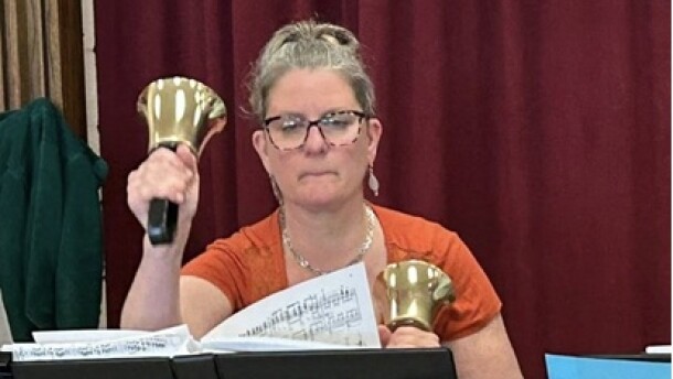 A person holds a hand bell in each hand while looking at sheet music