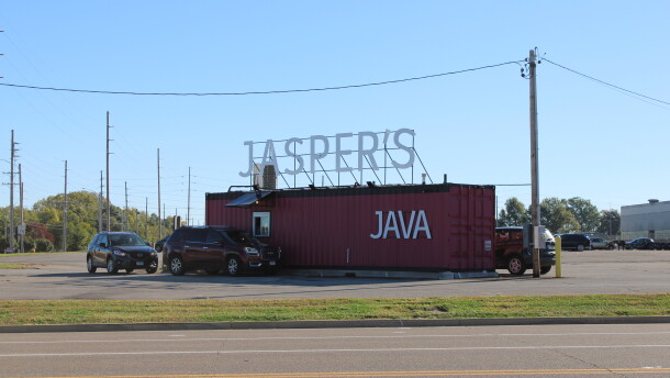 A shipping container converted into a double drive-thru coffee shop has at least three customers in line in their vehicles. 