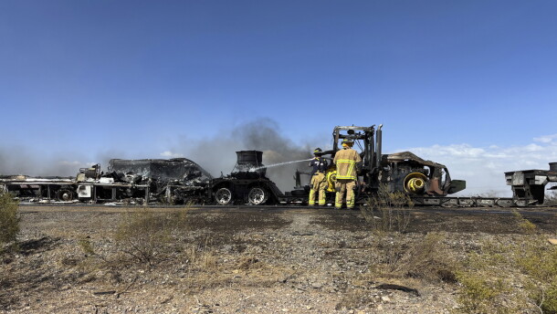 Firefighters hose water on burnt tractor-trailers and cars enveloped in smoke on a rural, desert highway in Arizona.