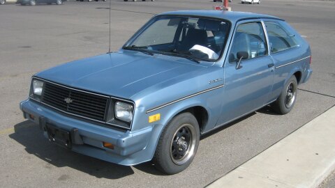 A light Blue three door Chervolet Chevette sits in a parking lot. 