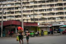 A woman and a child cross a street, with a residential high rise behind them. 