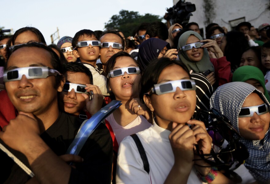 In this March 9, 2016 file photo, people wearing protective glasses look up at the sun to watch a solar eclipse in Jakarta, Indonesia.