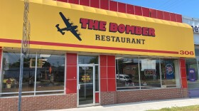 Outside the Bomber Restaurant. A yellow awning with "The Bomber" written in red lettering next to the image of a bomber airplane.