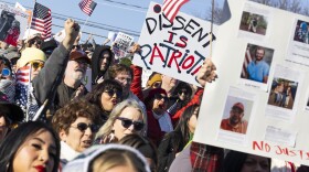 A large crowd holds up U.S. flags and signs at a protest.