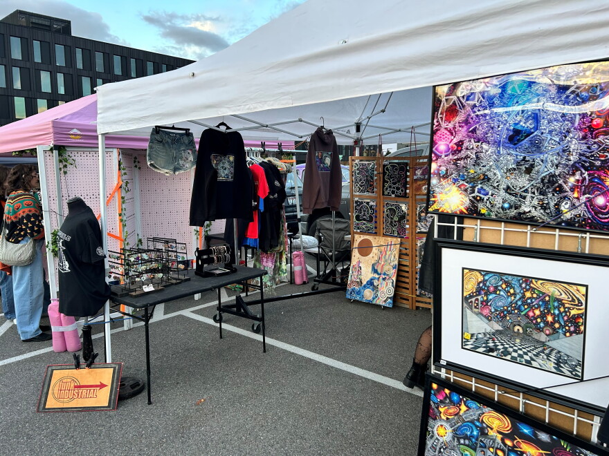 Colorful images, artwork and clothes hang in a vendor booth. 
