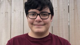 Galen is wearing a maroon shirt, square frame glasses, and fluffy hair while smiling at the camera.