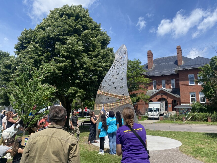 Youth members of Burlington's King Street Center join Mayor Emma Mulvaney-Stanak cut a large ribbon wrapped around a sculpture of a bird 
