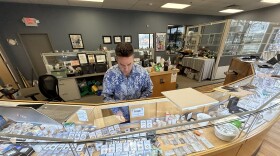 Geoffrey Demis, co-owner of Ferris Coin & Jewelry near Albany, reaches into his bullion display case at his shop a few miles from the state Capitol.