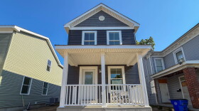 A two story home with a white porch and blue grey vinyl siding.