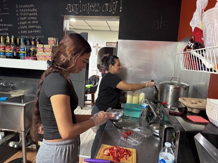 Two women prepare food in a busy kitchen.
