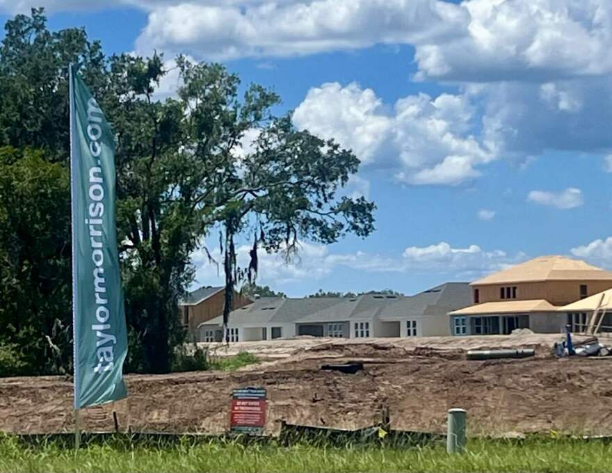 A flag in front of a construction site with dirt. There are houses being built in the background. 