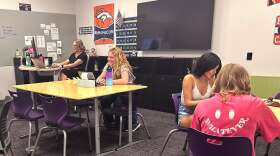 Students sit in a classroom with some behind laptops.
