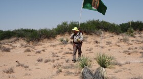 James Holeman communicates with volunteers using a handheld radio. He carries a Virgen de Guadalupe flag attached to his backpack.