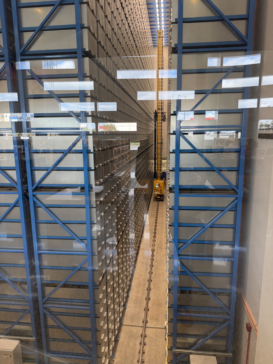 Tall blue steel racks of storage bins inside the Central Library's automated book retrieval system, seen through glass
