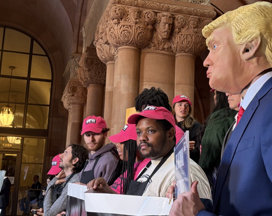 Food service workers from across New York joined lawmakers at the statehouse Monday, Jan. 27, 2025, to push for a bill that would nix the “subminimum wage” that workers currently receive, and require employers pay the full minimum wage on top of tips. An organizer from labor rights group One Fair Wage wore a mask of President Donald Trump to criticize his alleged support of large corporations that poorly treat service workers.