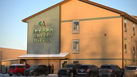 People stand outside a hotel with cars are parked in front