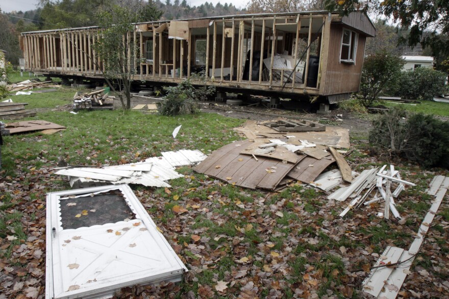 A white metal screen door lies in the foreground, in a photo of debris stripped off a mobile home during Tropical Storm Irene. The scene is of the aftermath, and shows the home in demolition.