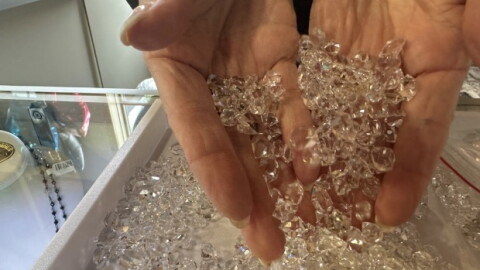A woman's hand scoops up a tray full of diamond looking stones that are actually Herkimer Diamond quartz.