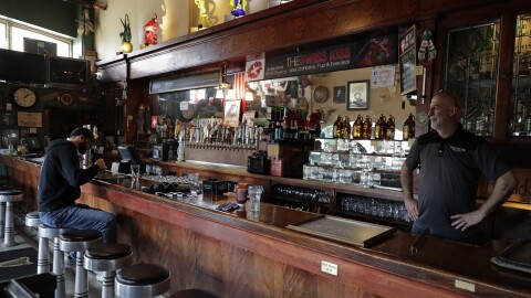 A man sits and eats at a bar as a bartender stands behind it. 