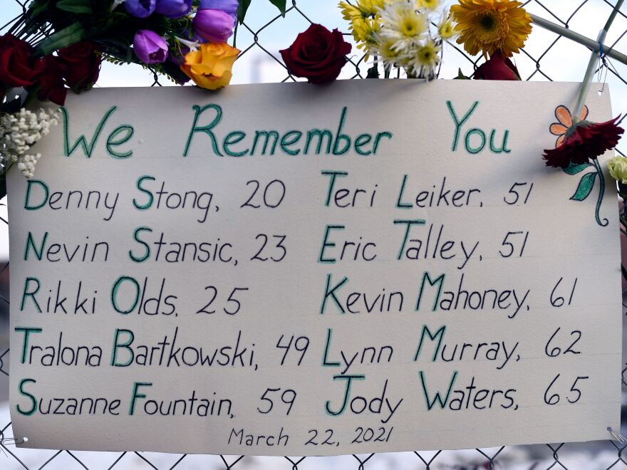 A sign framed with flowers lists the victims' names on the fence outside a King Soopers grocery store in Boulder, Colo. The suspected gunman made his first court appearance on Thursday.