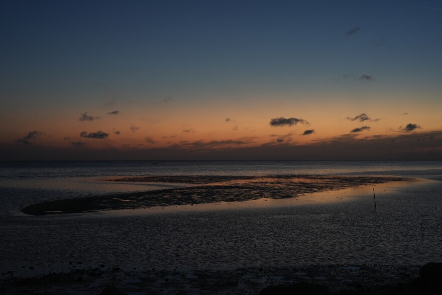 A sunset sky reflects off of water surrounding a sandbar 