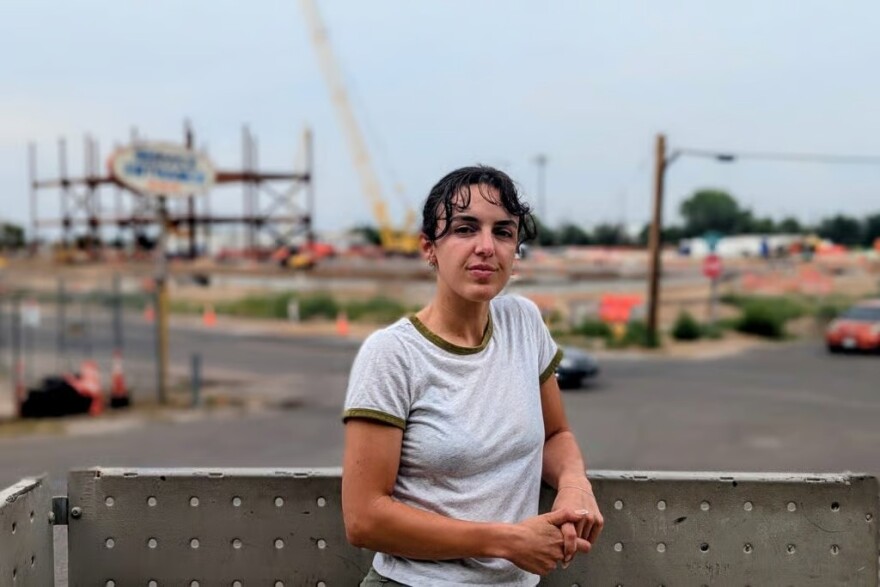 A woman leans against a short wall looking straight into the camera.