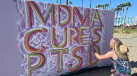 Andrew Patalano spray paints "MDMA cures PTSD" on May 22, 2021, in Venice Beach, California.  (Tonya Mosley/Here & Now)