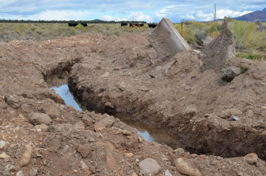 Concrete refuse sits askew in a dirt pile next to an irrigation ditch.