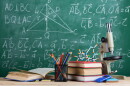 Education and sciences concept - books, molecule model and microscope on the desk in the auditorium, chalkboard background.
