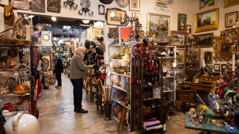 People look at objects in a store that is crowded with antique looking items.