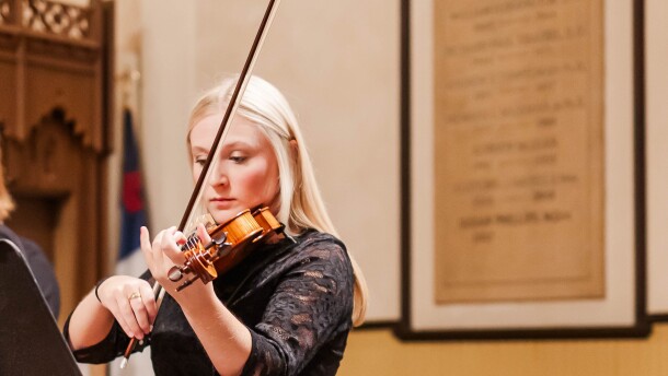 A picture of local musician Meredith Crifasi playing violin. She is wearing all black. 