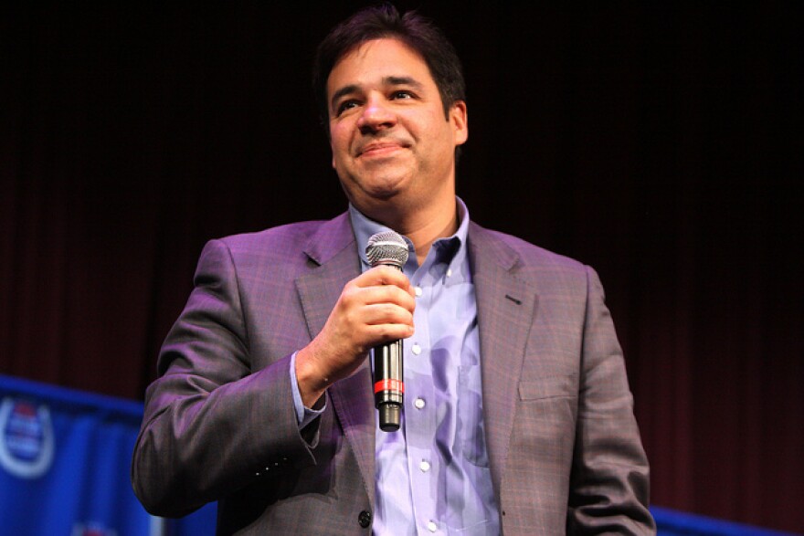 Raúl Labrador holds a microphone in his left hand, wearing a grey blazer with a light plaid pattern over a light blue oxford shirt