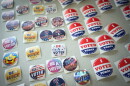 Close up image of about 30 different lapel stickers lying flat on a table. Some read "I Voted Today" with a red, white and blue design. Others read "Be a Voter" in colorful designs.