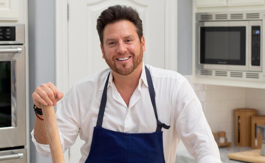 Chef Scott Conant stands in a kitchen with a rolling pin in hand. 