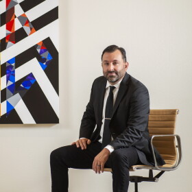 Scott Malbaurn sits beside a geometric painting with black-and-white stripes and colorful triangles.