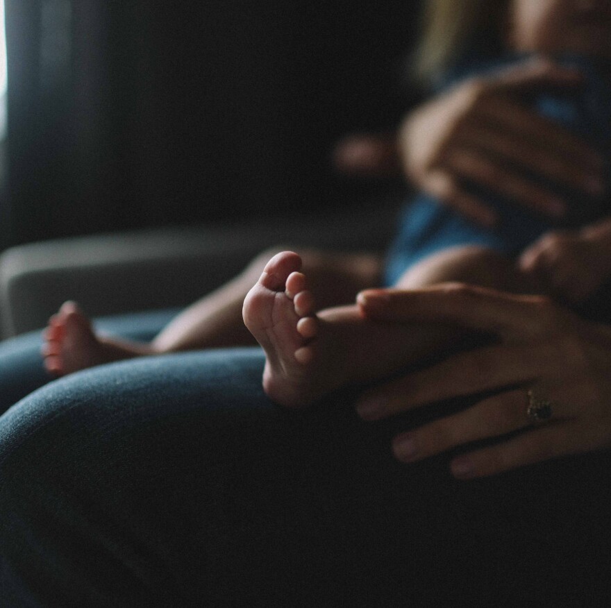 A baby is sitting on a woman's lap. The baby's feet and the woman's hand are in the foreground.