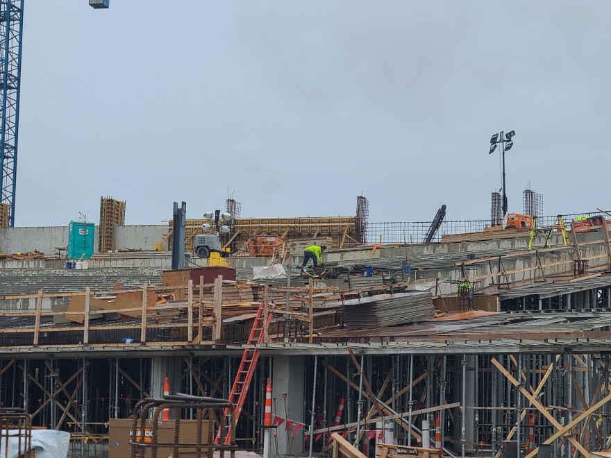 trabalhador da construção civil carrega algo que parece vergalhão em um canteiro de obras.