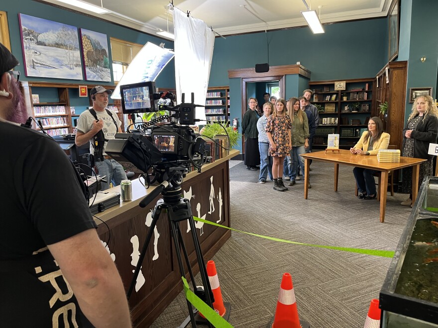 A film crew filming a scene in a library with students and teachers.