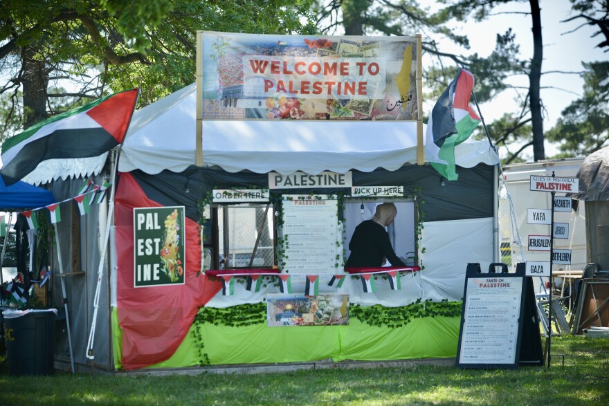 A white tent is decorated in Palestinian decorations. A woman is working inside the booth.