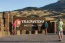A man takes a picture of two women standing in front of an entrance sign with the words “Yellowstone National Park.”