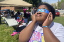 Layla Henry, 10, tries out specialized glasses while she waits for the eclipse outside of the Malloy/Jordan East Winston Heritage Center Monday. PAUL GARBER/WFDD