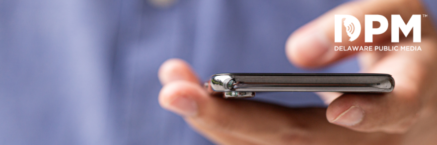 Hands holding a smartphone with the DPM Mobile App displayed on the screen. Text to the left of the image reads: The Delware Public Media Mobile App
