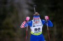 A woman cross-country skis in a race bib, with a rifle strapped to her back.