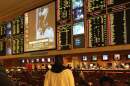 The back of a man is shown as he watches a football game in a sports betting room. 
