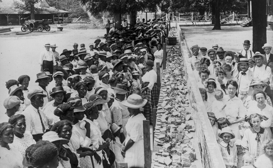 Crowds of African-American and white people are separated by a long counter covered with slices of bread at F.M. Gay's annual barbecue, held on his plantation every year in Alabama.