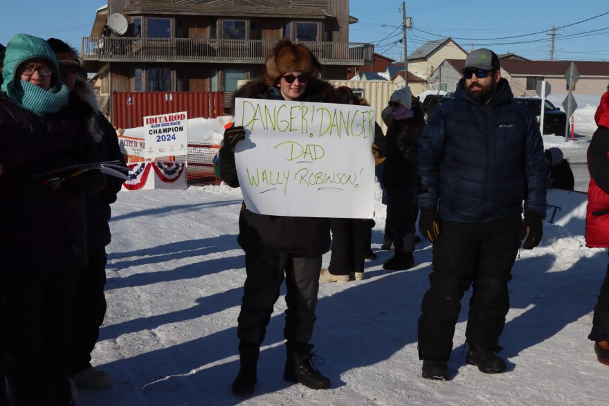 Junior Iditarod champion Emily Robinson holds a sign for her father, Wally, as he mushed to Nome and an 11th place finish in the Iditarod Trail Sled Dog Race on Wednesday, March 13, 2024.